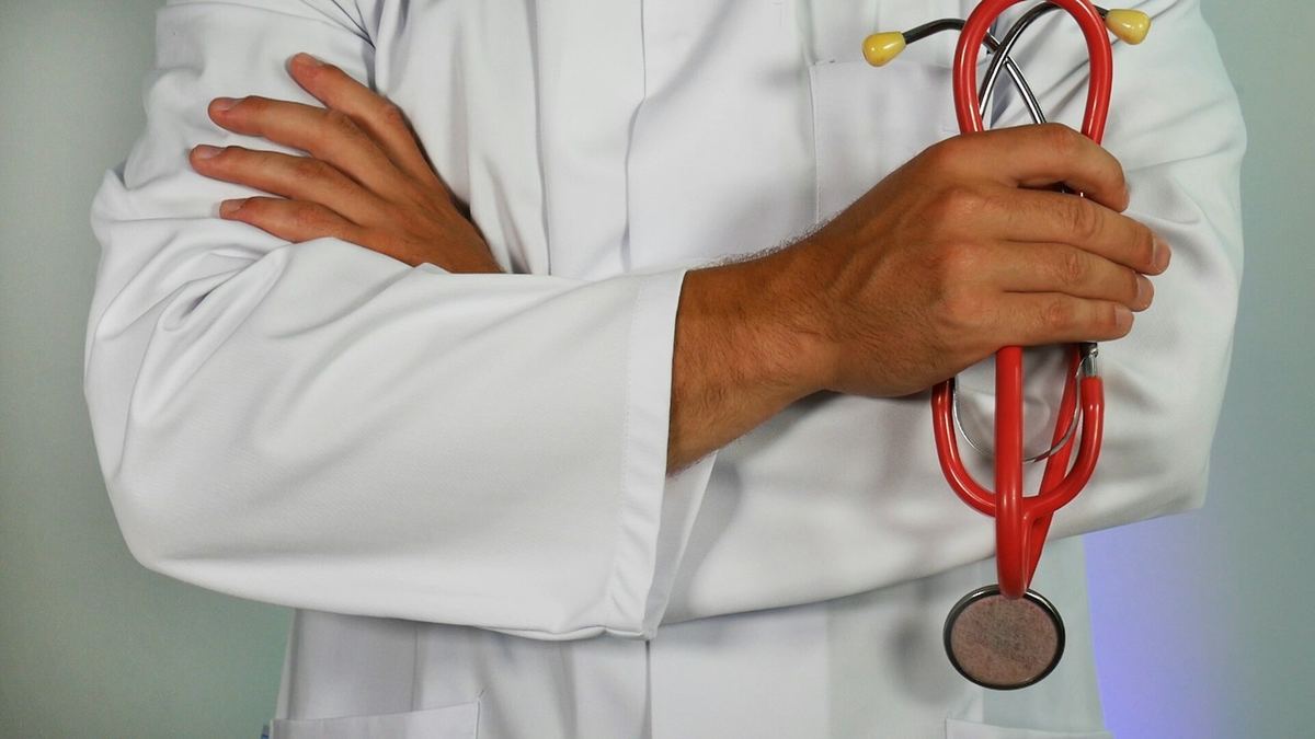 Médecin en blouse blanche, bras croisés, tenant un stéthoscope rouge