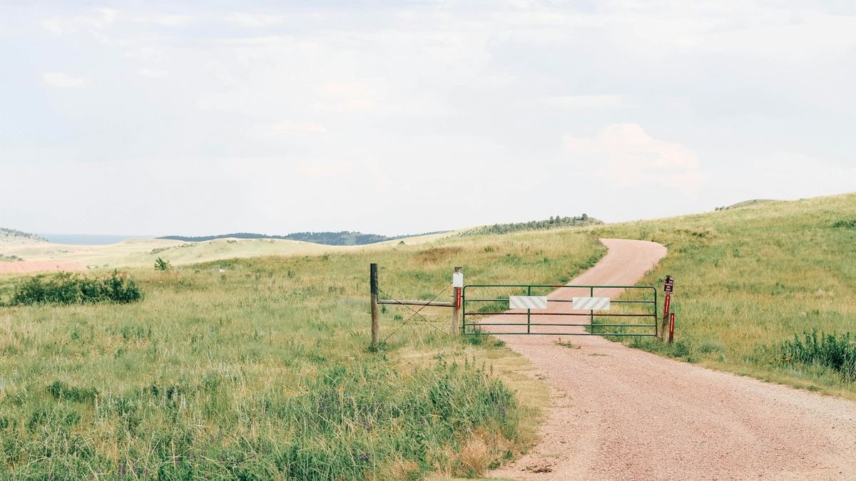 Chemin de terre traversant une prairie, fermé par une barrière